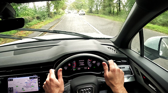 ands on a steering wheel inside a car, driving along a road